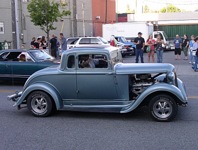 [This appears to be a cross between an early 20th century car and a rat rod. There are no side panels in the engine area exposing the engine and the air cleaner.]